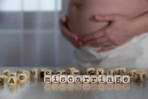 Word MISCARRIAGE composed of wooden letters. Word MISCARRIAGE composed of wooden letters. Pregnant woman in the background miscarriage stock pictures, royalty-free photos & images