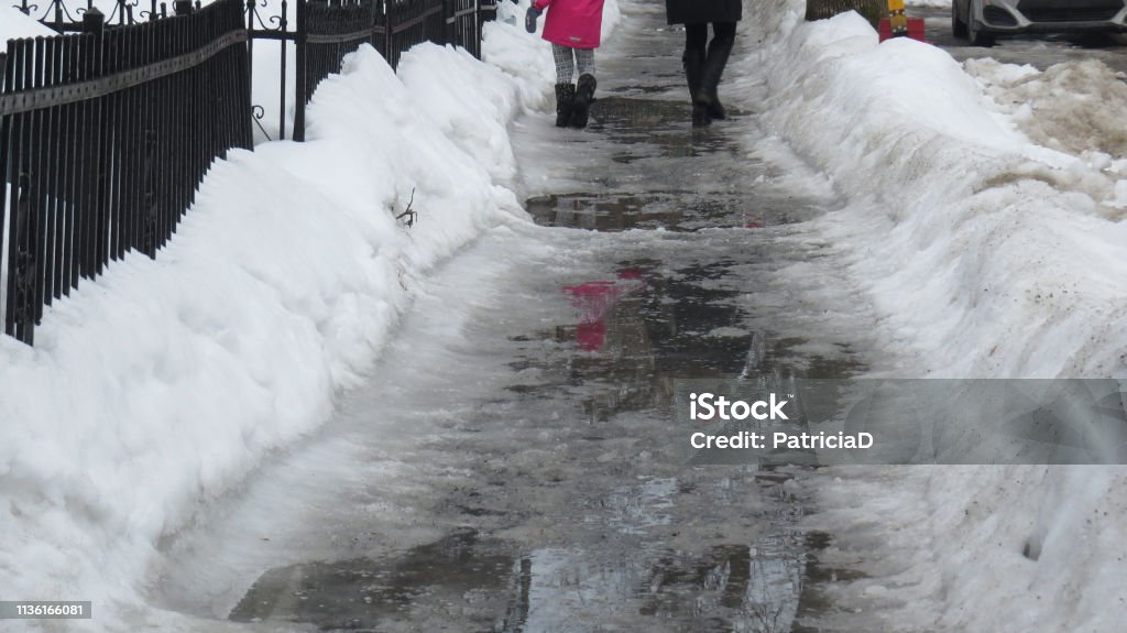 Mother and daughter walking on slushy slippery sidewalk in Montreal Mother and daughter walking on slushy slippery sidewalk, snow and ice melted, Montreal, Quebec, Canada Snow Stock Photo