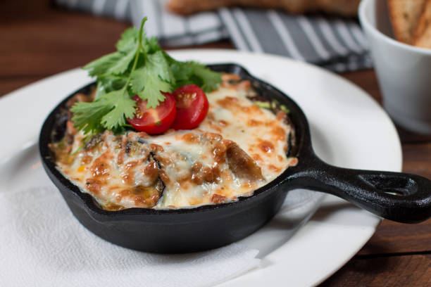 Grilled eggplant stuffed with tomatoes, nuts, pomegranate and herbs and cheese, baked in a black pan. Wood background
