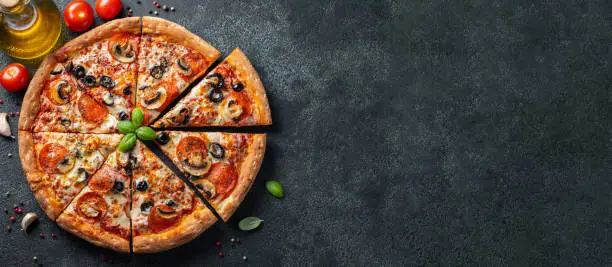 Tasty pepperoni pizza with mushrooms and olives on black concrete background. Top view of hot pepperoni pizza. With copy space for text. Flat lay. Banner.
