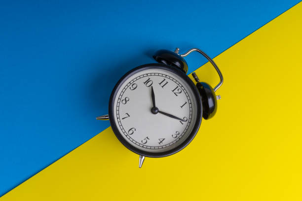 istock Black vintage alarm clock on a blue and yellow background 1136176552
