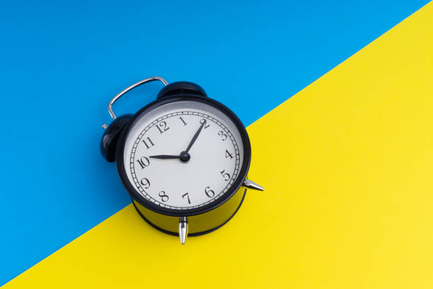 istock Black vintage alarm clock on a blue and yellow background 1136176554