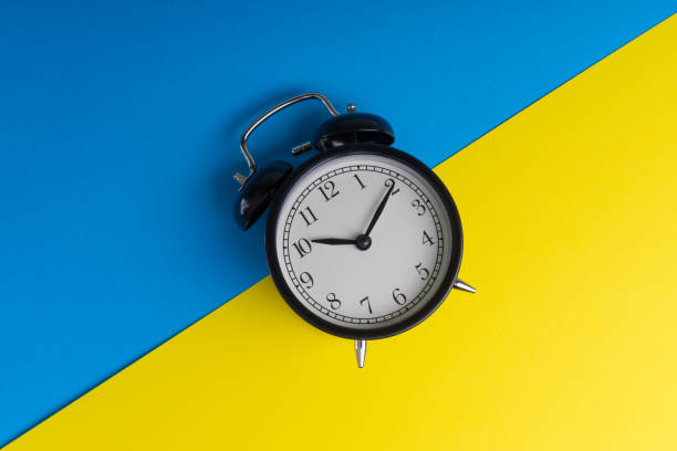 istock Black vintage alarm clock on a blue and yellow background 1136176559