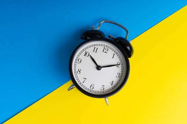 istock Black vintage alarm clock on a blue and yellow background 1136176562