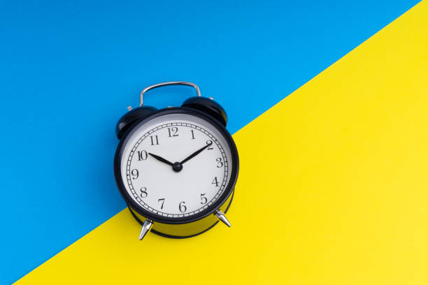 istock Black vintage alarm clock on a blue and yellow background 1136176573