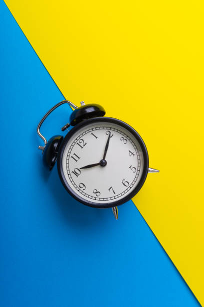 istock Black vintage alarm clock on a blue and yellow background 1136176579