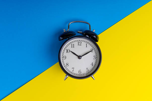 istock Black vintage alarm clock on a blue and yellow background 1136176580