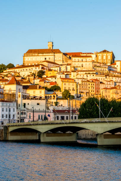 Sunset over Coimbra A riverfront view of the warm pastel colors of historical buildings stand out at sunset over the old Portuguese capital city of Coimbra, the Mondego river and the Santa Clara bridge. coimbra city stock pictures, royalty-free photos & images