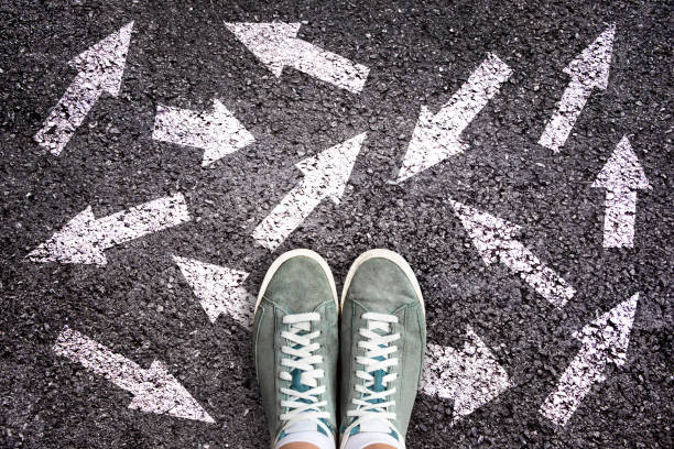 chaussures et flèches de sneaker pointant dans différentes directions sur le sol d'asphalte, concept de choix - prefer photos et images de collection