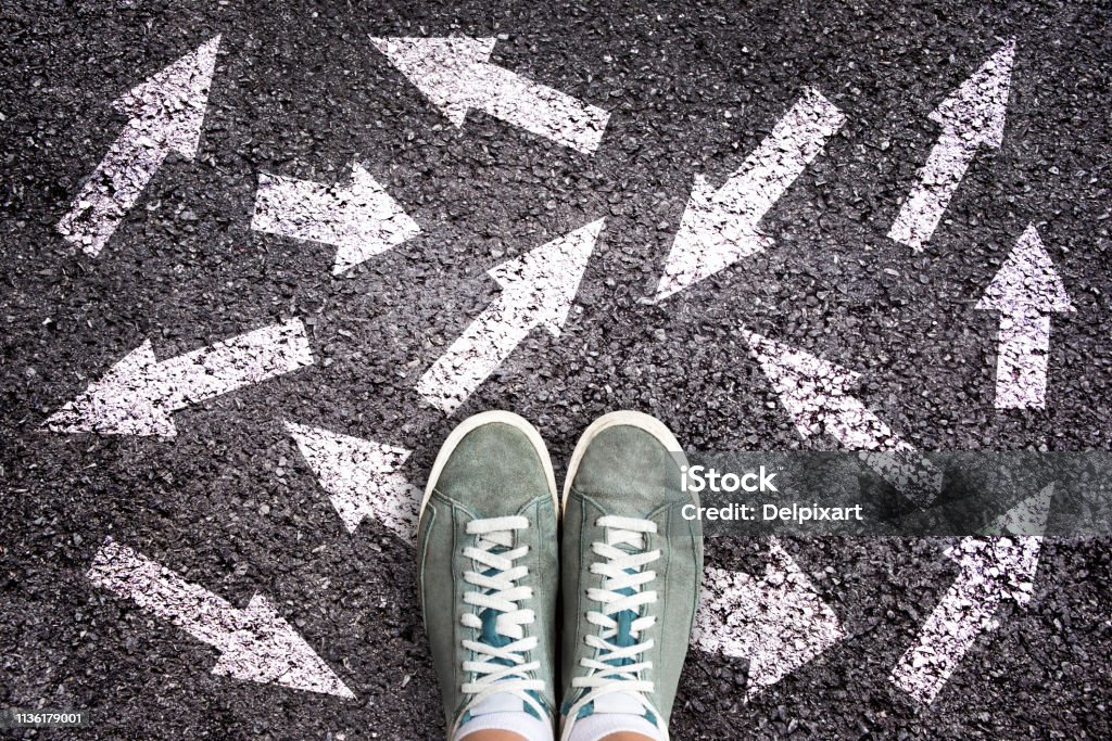 Sneaker shoes and arrows pointing in different directions on asphalt ground, choice concept Occupation Stock Photo