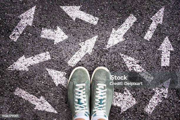 Sneaker Shoes And Arrows Pointing In Different Directions On Asphalt Ground Choice Concept Stock Photo - Download Image Now