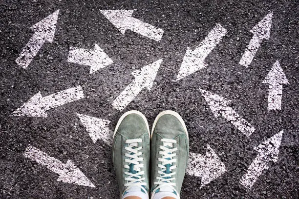 Sneaker shoes and arrows pointing in different directions on asphalt ground, choice concept