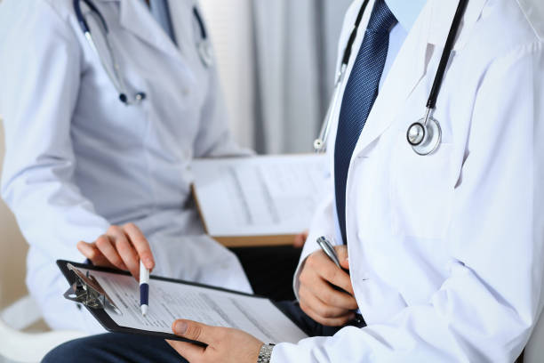 istock Two unknown doctors filling up medical form on clipboard, just hands closeup. Physicians asking question to patient or discussing medication program. Healthcare, insurance and medicine concept. 1136181202