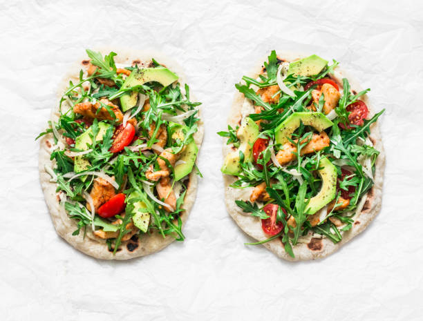 istock Pan-fried flatbread chicken, avocado, tomatoes, arugula pizza on a light background, top view 1136183194