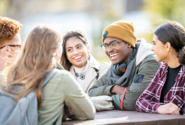 Friends on campus Five young adults are sitting at a picnic table outside on a fall day. They are smiling and chatting. 18 19 years photos stock pictures, royalty-free photos & images