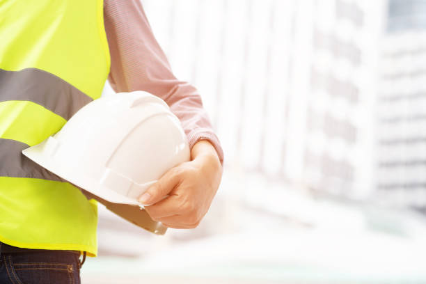 istock Close up front view of engineering male construction worker holding safety white helmet and wear reflective clothing for the safety of the work operation. outdoor of building background. 1136188290