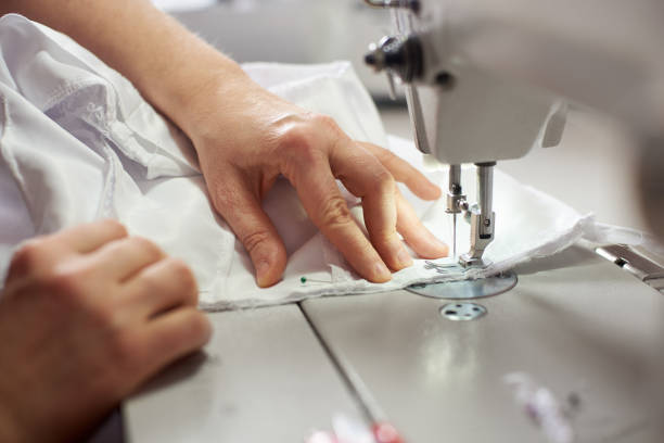 istock Female hands at sewing process and repairing white fabric on professional manufacturing machine. Close up view. 1136190196