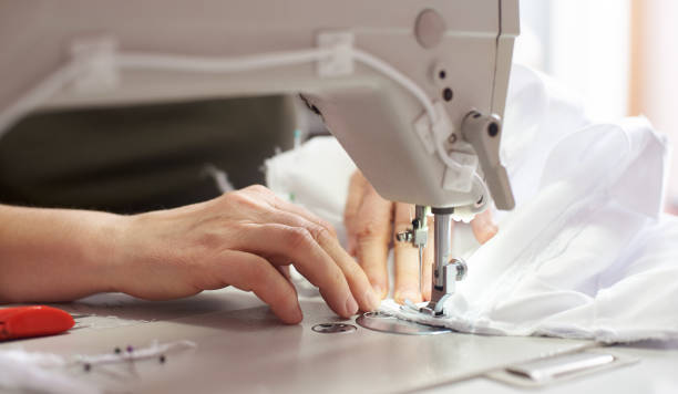 istock Female hands at sewing process and repairing white fabric on professional manufacturing machine. Close up front view. 1136190202