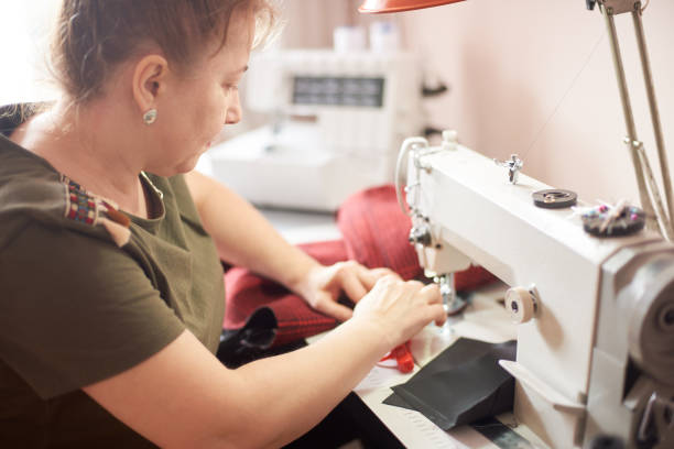 istock Female dressmaker stitching garment at her workplace in atelier using sewing machine. Side close up view 1136190241