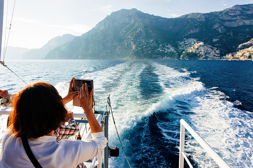Positano, Italy - September 30, 2017: Tourist taking photos on camera during cruise excursion tour on boat in Tyrrhenian Sea in Positano town of Amalfi Coast, Italy, summer.