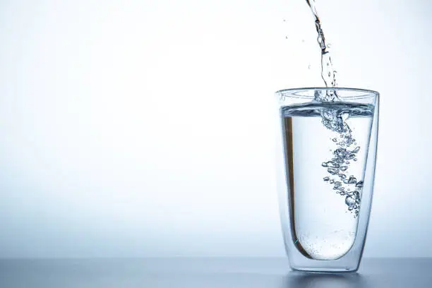 Man filling water from the blue plastic bottle into double glass.  Lighting set up shot on white background.  Concept of good health and refreshment.