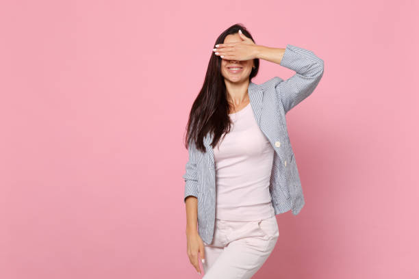Portrait of smiling young woman in striped jacket standing, covering eyes with hand isolated on pink pastel wall background in studio. People sincere emotions, lifestyle concept. Mock up copy space. Portrait of smiling young woman in striped jacket standing, covering eyes with hand isolated on pink pastel wall background in studio. People sincere emotions, lifestyle concept. Mock up copy space hair covering eyes stock pictures, royalty-free photos & images