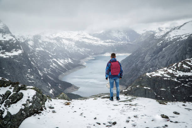 istock Man traveller with backpack standing back on edge and looking at scenery mountain landscape under snow, Trolltunga, Norway in may. 1136205329