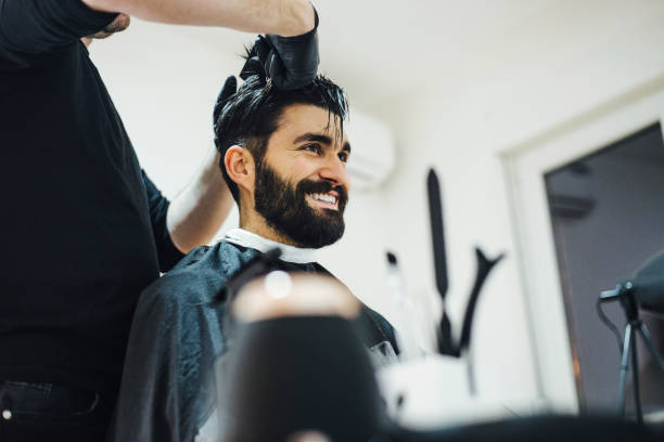 Young stylish barber with mustache and tattoos giving man haircut stock photo
