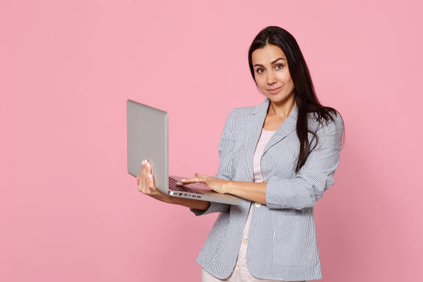 istock Portrait of smiling charming young woman in striped jacket using laptop pc computer isolated on pink pastel wall background in studio. People sincere emotions, lifestyle concept. Mock up copy space. 1136206815