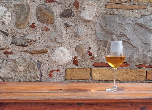 Glass of amber white wine on a rustic wooden table with an old stone wall behind. Background for copy space.