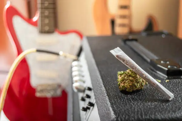 Photo of Music and marijuana, looking inspiration. Weed joint and big marijuana bud on guitar speaker. Musical instruments in the background with blur effect.