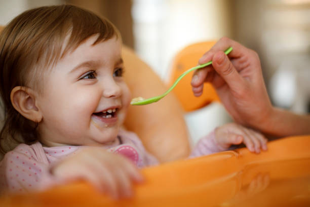 母はスプーンで幸せな幼児の女の子を養う - 動物の摂食 ストックフォトと画像