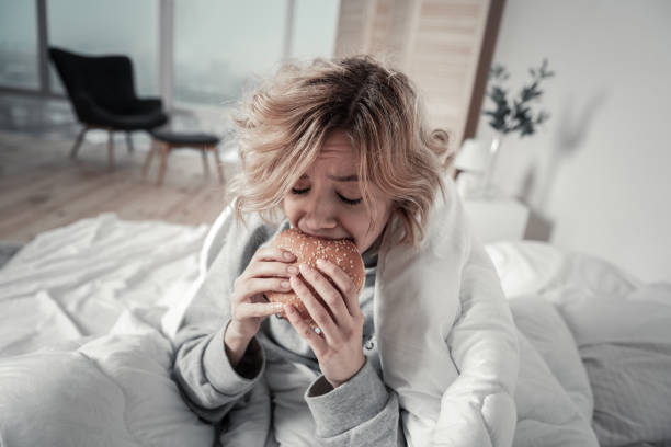 istock Woman biting burger while eating too much in depression 1136220873