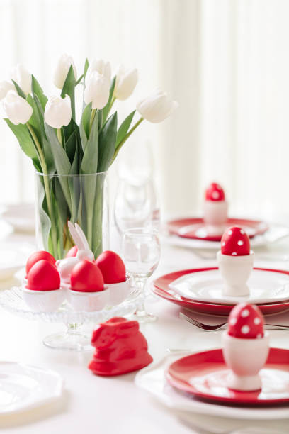 istock Happy easter. Decor and table setting of the Easter table is a vase with white tulips and dishes of red and white color. Easter colored eggs with white polka dots. 1136221102