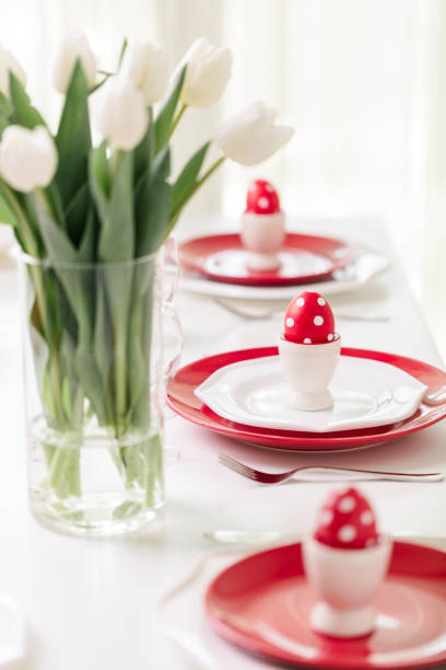 istock Happy easter. Decor and table setting of the Easter table is a vase with white tulips and dishes of red and white color. Easter colored eggs with white polka dots. 1136221109