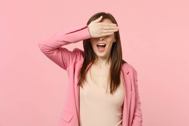 Cheerful funny young woman in jacket keeping mouth wide open, covering eyes with hand isolated on pastel pink wall background in studio. People sincere emotions, lifestyle concept. Mock up copy space. Cheerful funny young woman in jacket keeping mouth wide open, covering eyes with hand isolated on pastel pink wall background in studio. People sincere emotions, lifestyle concept. Mock up copy space hair covering eyes stock pictures, royalty-free photos & images