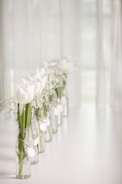 White tulips in bottles with Easter decoration in the form of eggs on a white table. Selective focus.