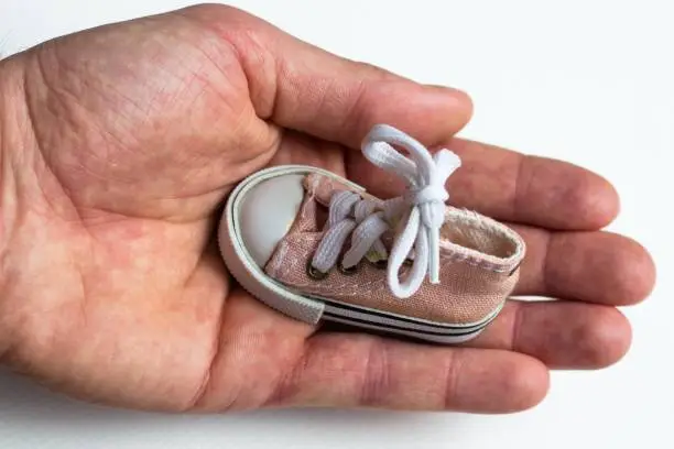 Photo of In a large and strong male hand is a small children's shoes. On shoes tied with a bow bow. A hand with shoes on a white background that highlights them.