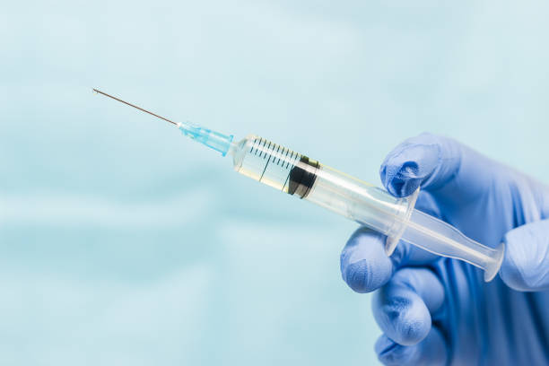 istock Blue gloved hand holding a syringe on blue background 1136229040