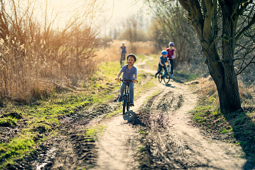 Kids with mother riding bicycles on dirt road on early spring day.
Nikon D800