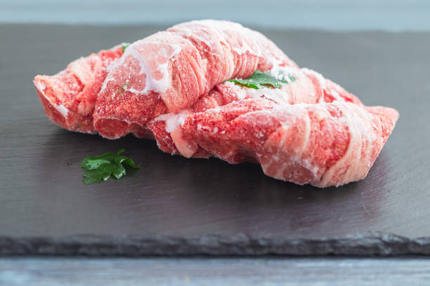 Frozen meat with parsley on a black slate board. Close-up, selective focus