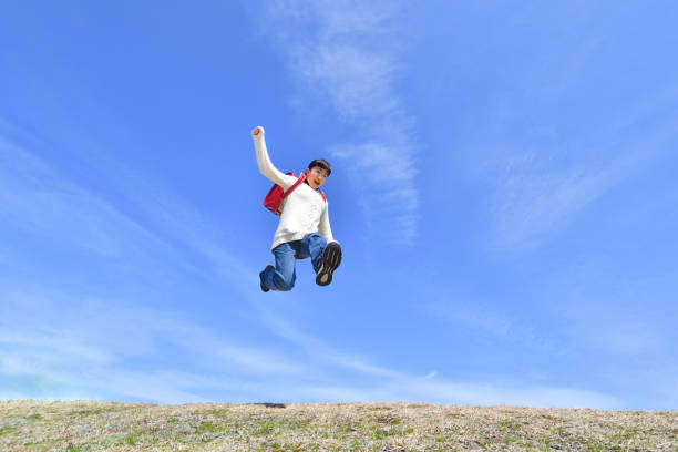 istock Japanese elementary school girl jumping in the blue sky 1136238769