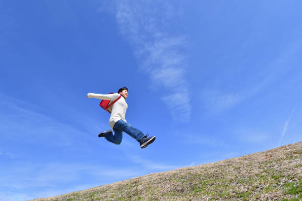 istock Japanese elementary school girl jumping in the blue sky 1136238772