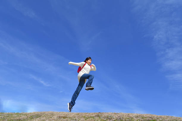 istock Japanese elementary school girl jumping in the blue sky 1136238806