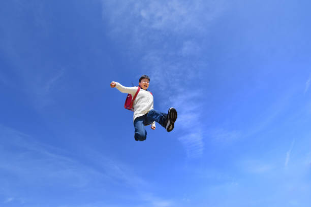 istock Japanese elementary school girl jumping in the blue sky 1136238857