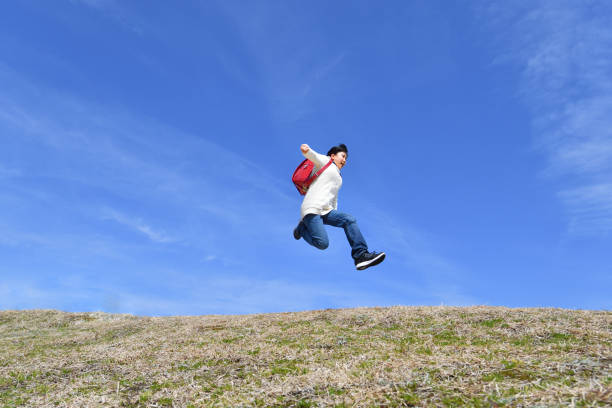 istock Japanese elementary school girl jumping in the blue sky 1136238880