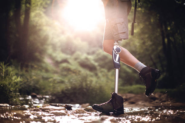 Man with disability crossing stream in forest Young Amputee Hiker Visiting Waterfalls, Walking Happily On Stream in forest on sunny day, unrecognizable person disabled person hiking outdoors stock pictures, royalty-free photos & images