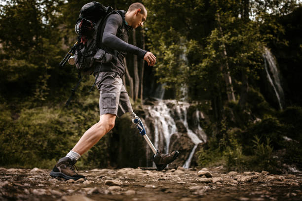 Man with disability crossing stream in forest Young Amputee Hiker Visiting Waterfalls, Walking Happily On Stream in forest disabled person hiking outdoors stock pictures, royalty-free photos & images
