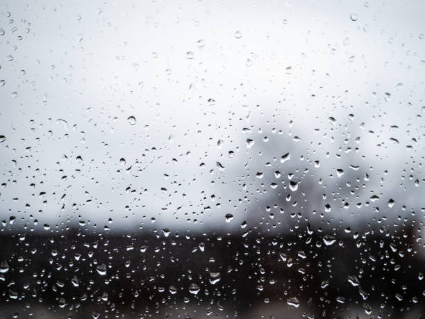 Water Drops on a window with grey skies and silhouettes of houses in background