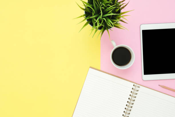 istock Office desk working space - Flat lay top view photo of working space with blank mock up tablet, coffee cup and notebook on pastel background. Pastel pink yellow color copy space working desk concept. 1136269313